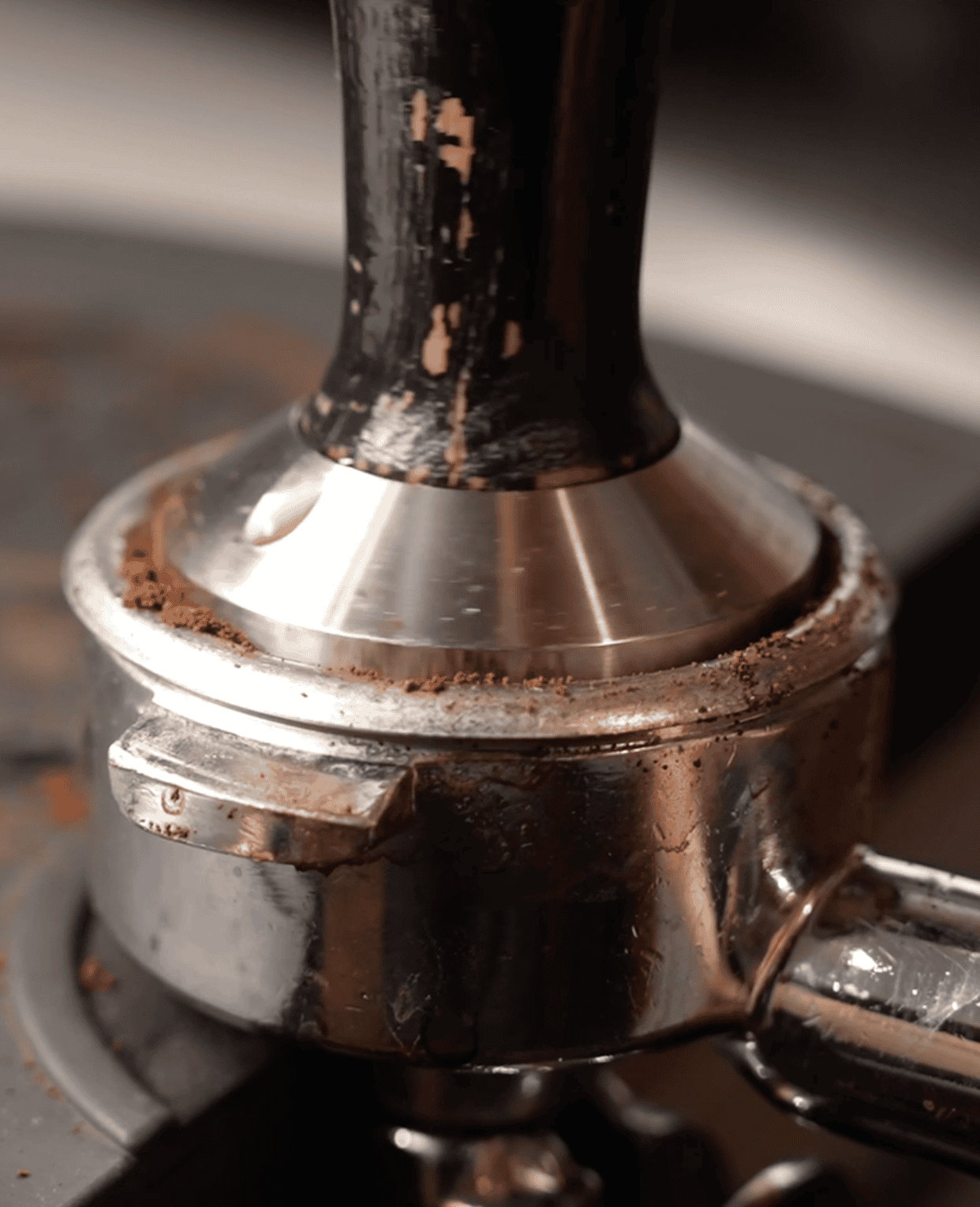 Close-up of espresso machine portafilter handle with coffee grounds.