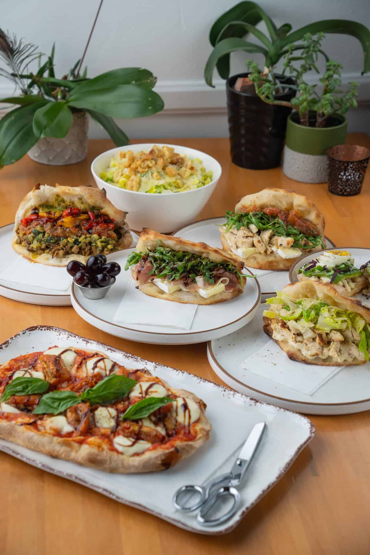 Vespa table spread with pinsa, filled sandwiches, salad, and olives